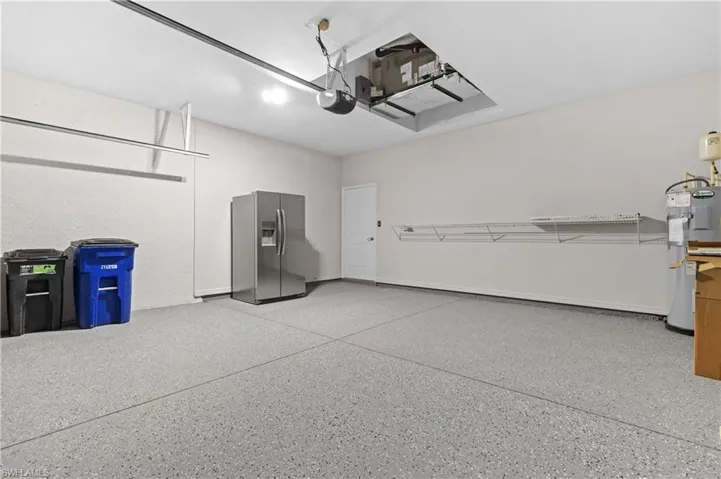 Garage with water heater, stainless steel fridge with ice dispenser, and a garage door opener