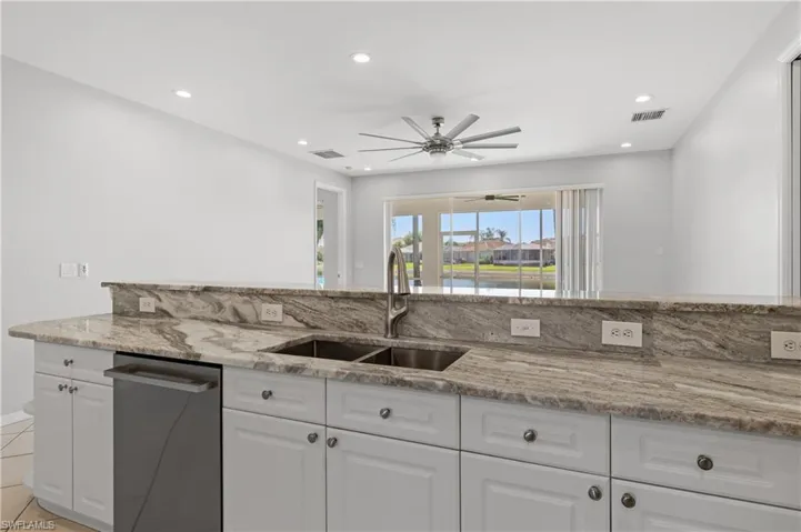 Kitchen featuring white cabinets, light stone countertops, stainless steel dishwasher, a ceiling fan, and recessed lighting