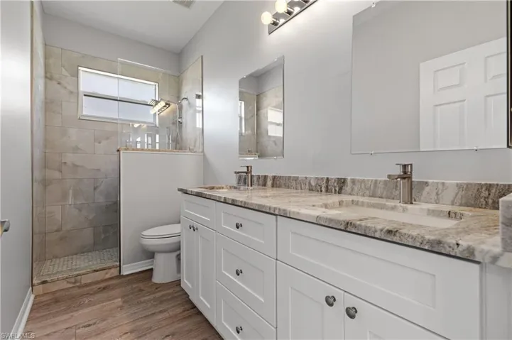 Bathroom featuring double vanity, walk in shower, and light wood-style floors
