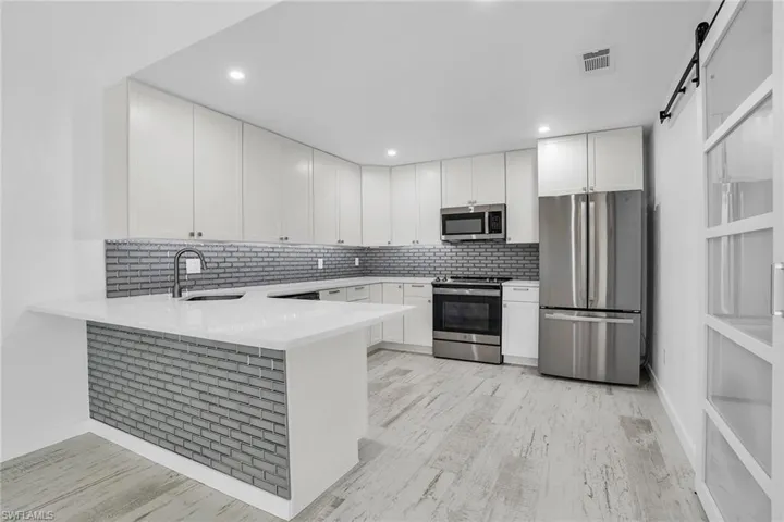 Kitchen featuring kitchen peninsula, stainless steel appliances, white cabinetry, a barn door, and light wood-type flooring