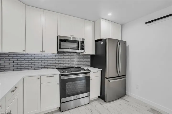 Kitchen featuring white cabinetry, light hardwood / wood-style floors, appliances with stainless steel finishes, light stone counters, and backsplash