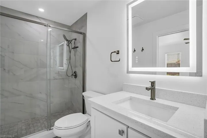 Bathroom featuring a shower with shower door, vanity, and toilet