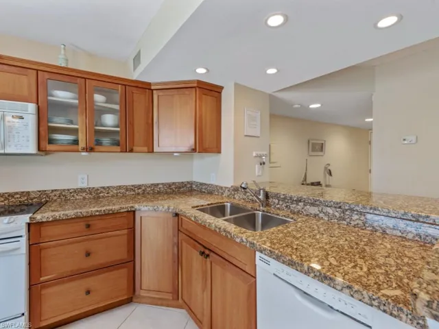 Kitchen featuring white appliances, brown cabinetry, recessed lighting, light tile patterned floors, and glass insert cabinets
