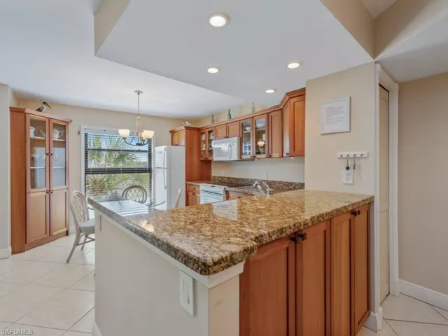 Kitchen with glass insert cabinets, light tile patterned floors, light stone counters, pendant lighting, and brown cabinets