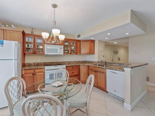 Kitchen featuring dark stone countertops, recessed lighting, white appliances, light tile patterned flooring, and brown cabinetry