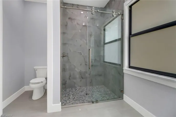 Bathroom featuring a shower with shower door, toilet, and tile patterned floors