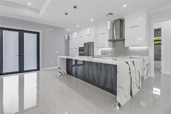 Kitchen featuring decorative light fixtures, light tile patterned flooring, wall chimney range hood, white cabinets, and appliances with stainless steel finishes