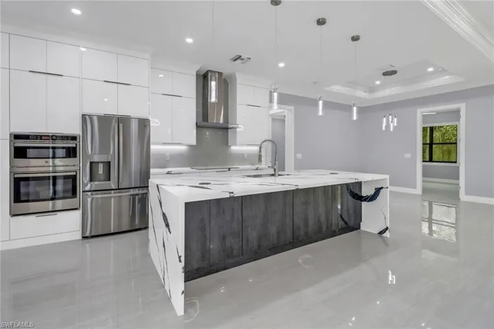 Kitchen featuring appliances with stainless steel finishes, white cabinets, a spacious island, and wall chimney exhaust hood