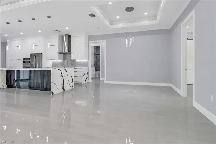 Kitchen featuring stainless steel appliances, hanging light fixtures, white cabinets, and wall chimney exhaust hood