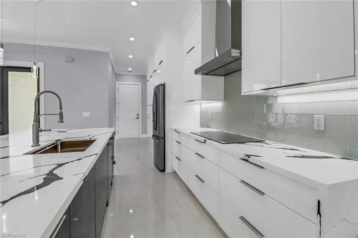 Kitchen with decorative light fixtures, white cabinetry, wall chimney range hood, light stone counters, and stainless steel refrigerator