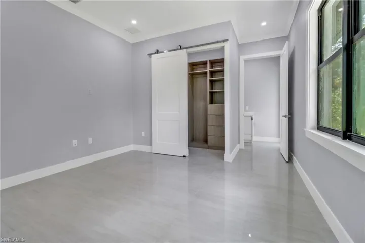 Unfurnished bedroom with a spacious closet, a closet, a barn door, light tile patterned flooring, and ornamental molding