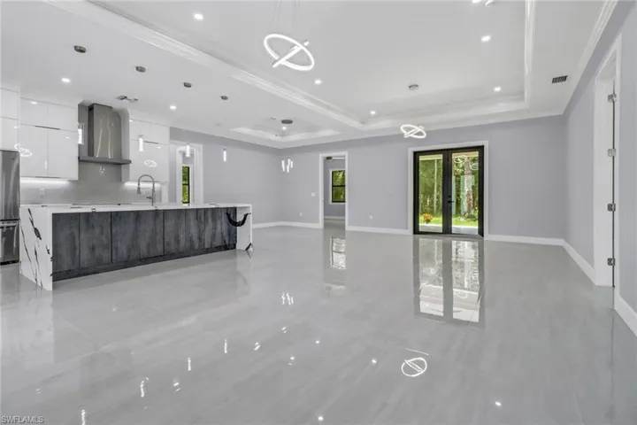 Kitchen featuring light tile patterned floors, wall chimney range hood, a large island, a tray ceiling, and hanging light fixtures