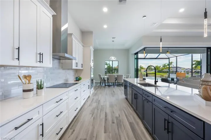 Kitchen featuring sink, white cabinets, wall chimney range hood, decorative light fixtures, and black electric cooktop