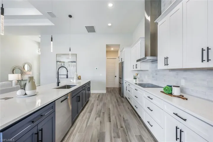 Kitchen featuring white cabinets, hanging light fixtures, sink, wall chimney exhaust hood, and appliances with stainless steel finishes