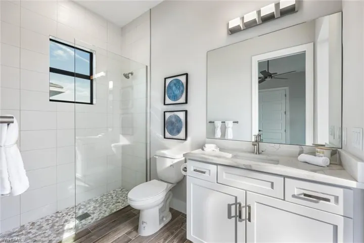 Bathroom with a tile shower, hardwood / wood-style flooring, ceiling fan, vanity, and toilet