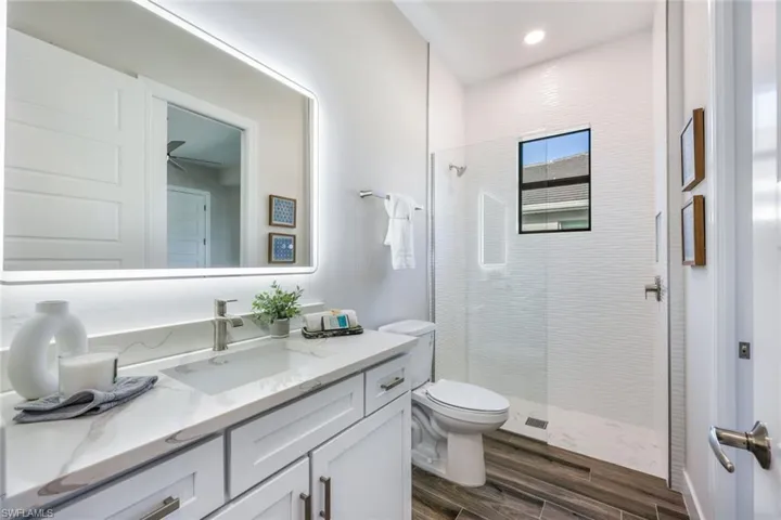 Bathroom featuring wood-type flooring, tiled shower, vanity, and toilet