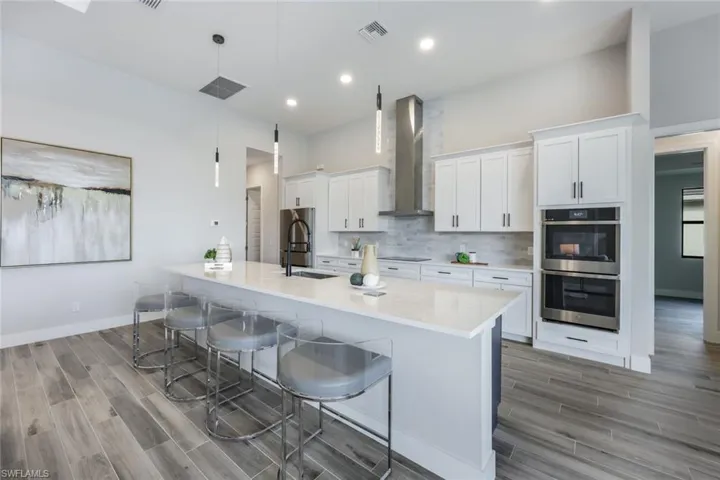 Kitchen featuring pendant lighting, a large island, and wall chimney range hood