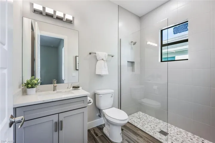 Bathroom with a tile shower, vanity, hardwood / wood-style floors, and toilet