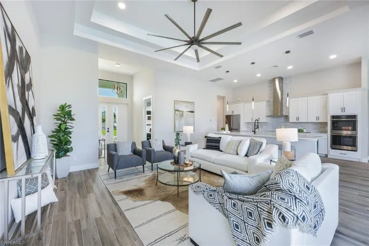 Living room with ceiling fan, sink, light wood-type flooring, and a raised ceiling