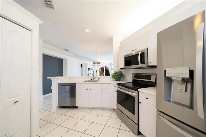 Kitchen with appliances with stainless steel finishes, a peninsula, light countertops, decorative light fixtures, and white cabinetry