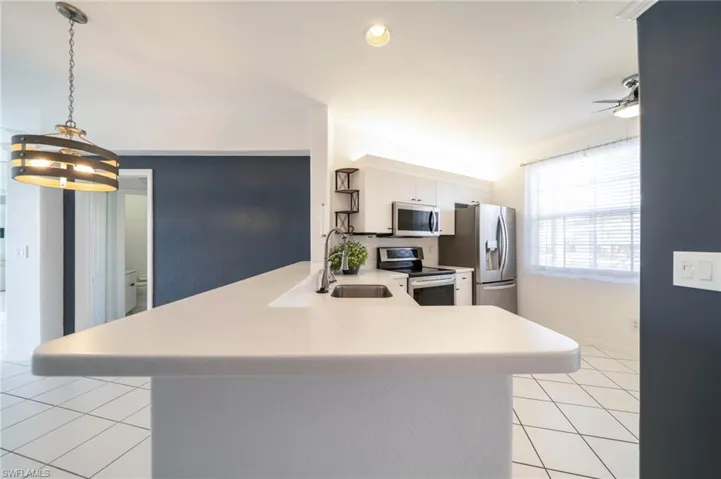 Kitchen with appliances with stainless steel finishes, a peninsula, light countertops, light tile patterned floors, and decorative light fixtures
