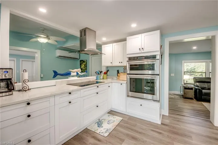 Kitchen featuring stainless steel double oven, white cabinets, island exhaust hood, light wood-style flooring, and recessed lighting