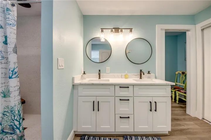 Bathroom with double vanity, tiled shower, and light wood-style floors
