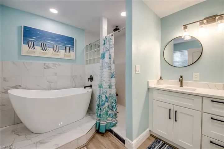 Bathroom with vanity, a freestanding bath, a tile shower, tile walls, and light wood-style flooring