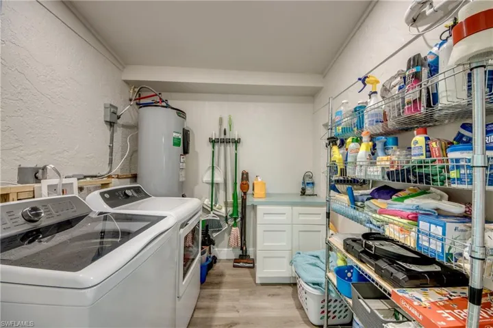 Washroom with a textured wall, light wood-type flooring, electric water heater, and separate washer and dryer