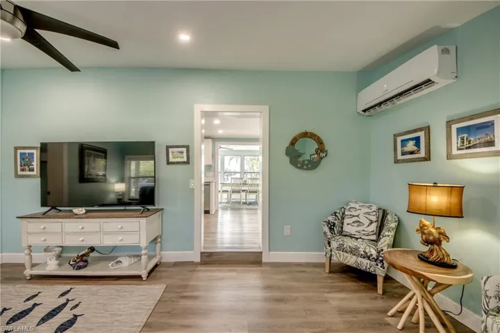 Living area with wood finished floors, an AC wall unit, ceiling fan, and recessed lighting