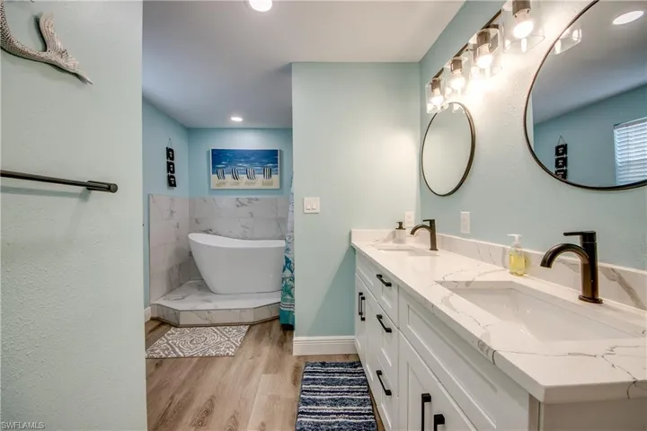 Bathroom with a freestanding bath, shower, light wood finished floors, double vanity, and recessed lighting