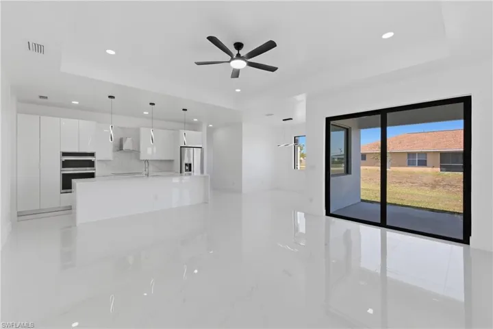 Unfurnished living room featuring a raised ceiling, a ceiling fan, recessed lighting, and light marble finish floors