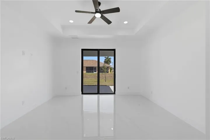 Empty room with a tray ceiling, light marble finish flooring, ceiling fan, and recessed lighting