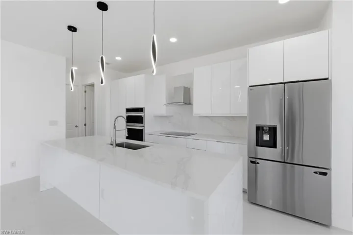 Kitchen featuring stainless steel appliances, white cabinets, light stone counters, a center island with sink, and hanging light fixtures