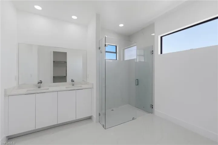 Full bathroom featuring a marble finish shower, double vanity, light marble finish flooring, recessed lighting, and a walk in closet