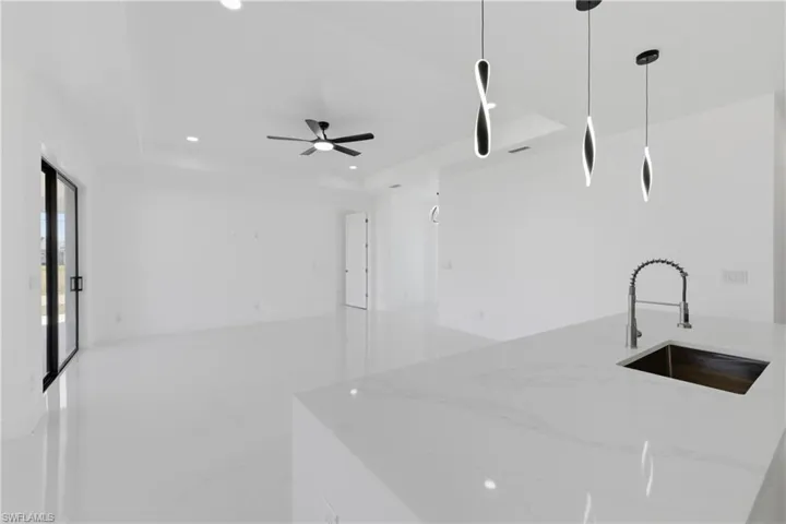Kitchen with light stone countertops, a tray ceiling, hanging light fixtures, a kitchen island with sink, and a ceiling fan