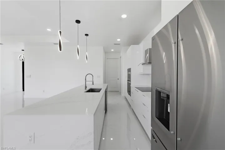 Kitchen featuring stainless steel fridge, modern cabinets, a kitchen island with sink, and light stone counters