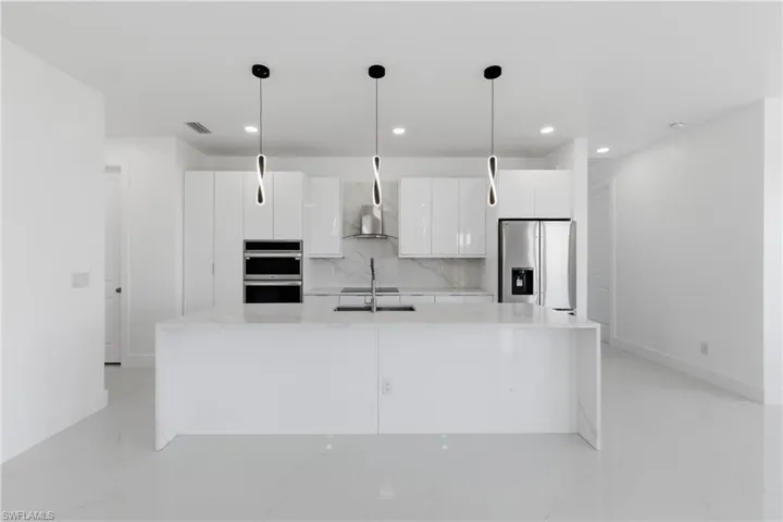Kitchen with white cabinetry, light stone countertops, stainless steel appliances, tasteful backsplash, and hanging light fixtures