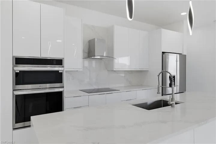 Kitchen featuring stainless steel appliances, white cabinets, range hood, light stone countertops, and modern cabinets
