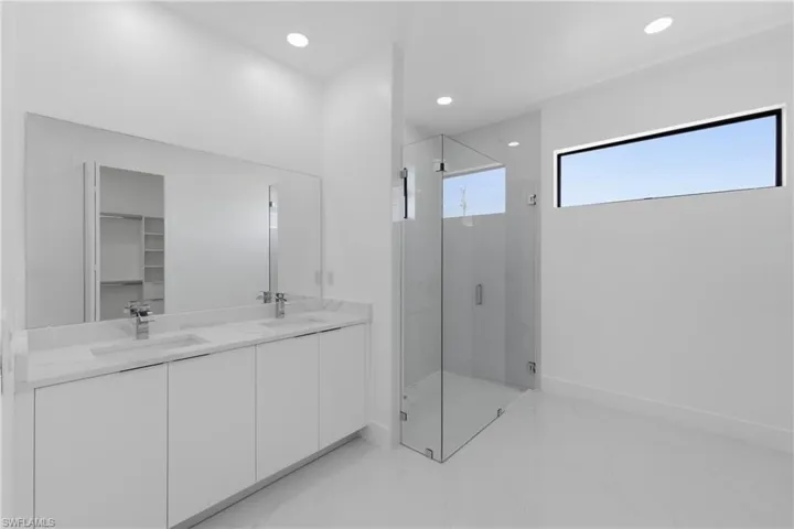 Bathroom featuring a marble finish shower, double vanity, recessed lighting, a spacious closet, and light marble finish floors