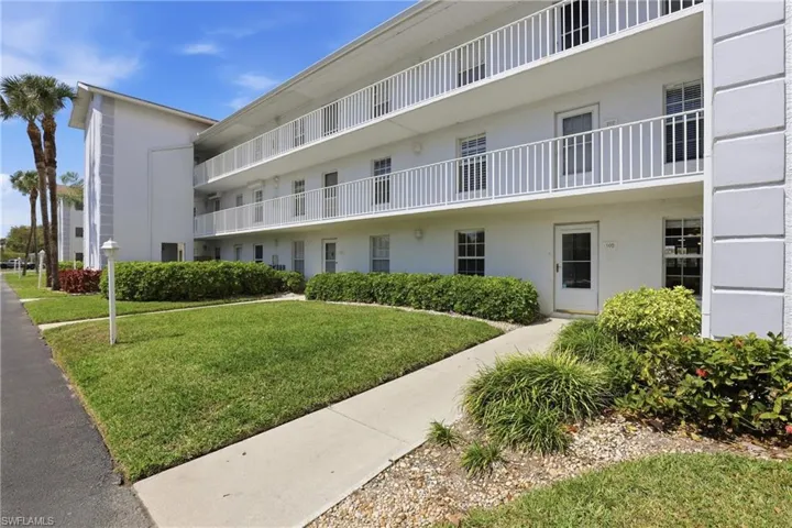The property features a white exterior, multiple balconies with white railings, and a well-maintained lawn with landscaping