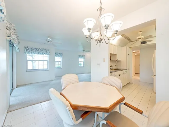 Carpeted dining room with ceiling fan with notable chandelier