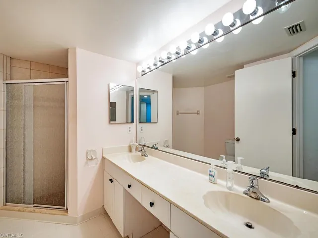 Bathroom with double vanity, tile flooring, and a shower with door