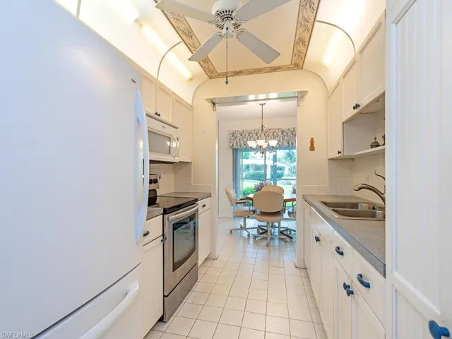 Kitchen featuring white appliances, backsplash, light tile floors, sink, and white cabinets
