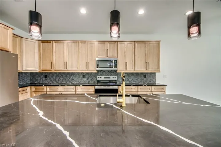 Kitchen with light brown cabinets, appliances with stainless steel finishes, and pendant lighting