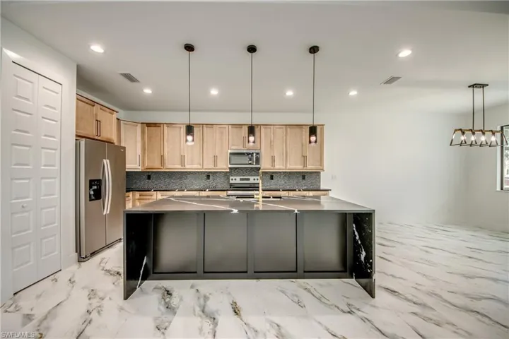 Kitchen featuring stainless steel appliances, a kitchen island with sink, backsplash, pendant lighting, and light tile flooring