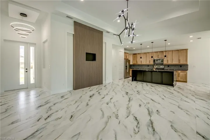 Kitchen with hanging light fixtures, stainless steel appliances, a kitchen island with sink, and light tile floors