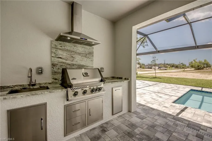 View of patio featuring glass enclosure, sink, and area for grilling