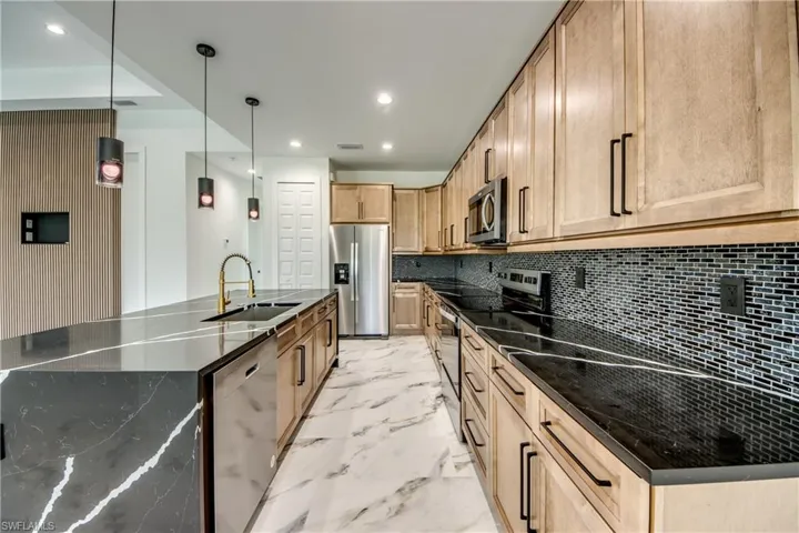 Kitchen featuring tasteful backsplash, stainless steel appliances, decorative light fixtures, light tile floors, and a kitchen island with sink