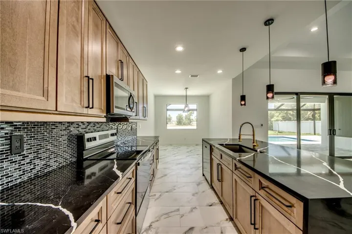 Kitchen with stainless steel appliances, light tile flooring, backsplash, hanging light fixtures, and sink
